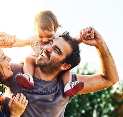 A man lifts a child in the air while a woman looks on.