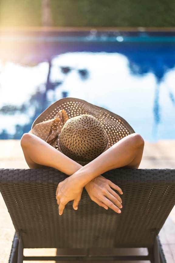 A woman in a hat is sitting on a chair by the pool at Mila Apartments, Ellisville, MO, 63011