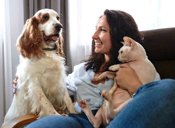 A woman is sitting on a couch holding a dog and a cat.