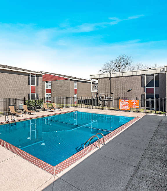 A pool area with sun loungers and a building in the background.