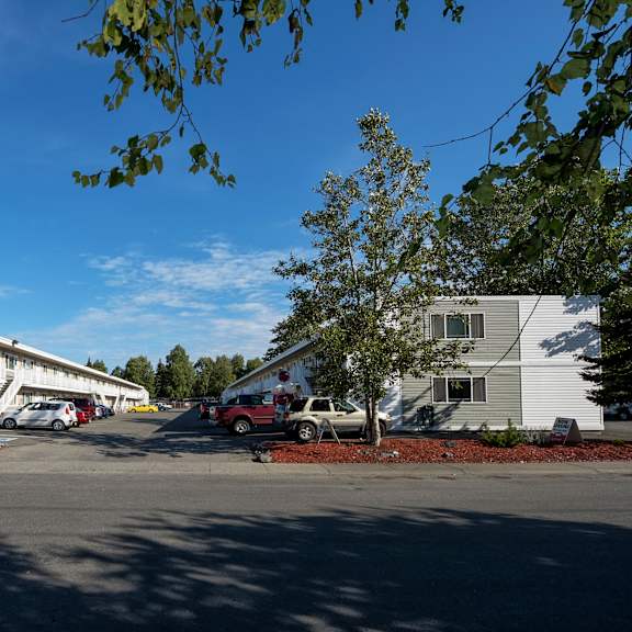 A parking lot with cars and trees in front of apartment buildings.