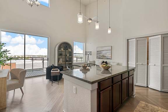 A modern kitchen with a large island and a balcony with a view of the sky.
