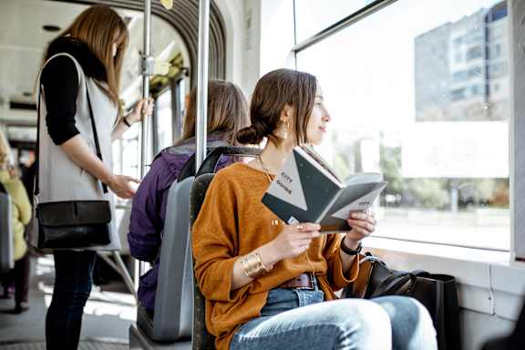 A woman in a yellow sweater is reading a book on a bus.
