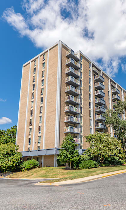 A tall building with a lot of windows and balconies is surrounded by trees and bushes.