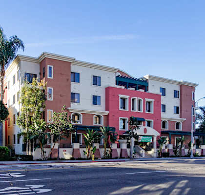 A multi-story building with a red and beige facade is surrounded by palm trees.