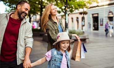A man and a woman are holding hands with a child who is holding a shopping bag.