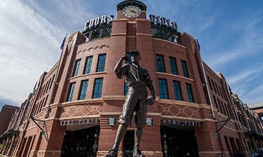 A statue of a baseball player stands in front of a red brick building with the word  at Waterford RiNo Apartments, Colorado