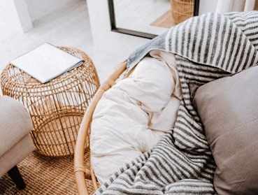 A wicker ottoman with a white cushion sits next to a striped couch.