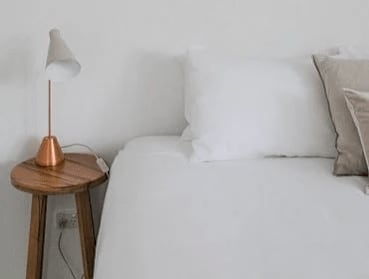 A bed with white pillows and a lamp on a wooden stool.