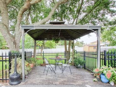 outdoor pavillion with seating under a canopy beside iron fence with potted plants