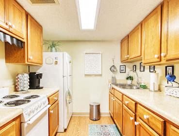 Galley kitchen with wood cabinetry, ample counter space, and white appliances