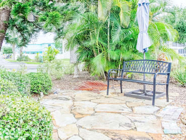 outdoor patio area of flagstone with metal bench, umbrella, and lush plant life