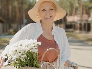 a woman in a hat is holding a bike and a basket of flowers