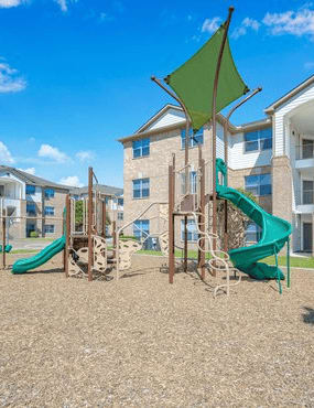 A playground with a green slide and a wooden swing set.