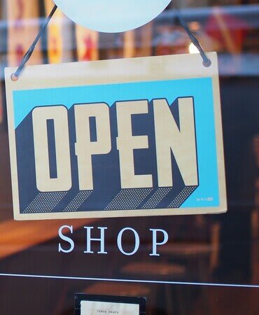A sign that says "OPEN SHOP" is hanging in front of a window.