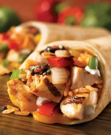 A close-up of a chicken wrap with vegetables and sauce on a wooden surface.