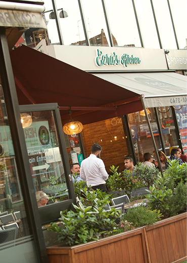 A restaurant with a red awning and people sitting at tables outside.