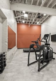 fitness center with cardio machines, free weights, TV, and large mirror at Brooke Street Lofts in Fond du Lac