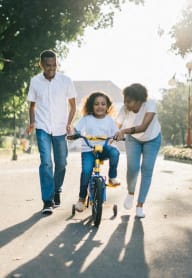 a young girl riding a bike down the street with her family