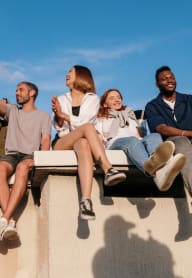 a group of diverse friends sitting on a ledge and smiling in front of a blue sky