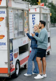 a man and woman standing in front of a hot dog food truck in New York