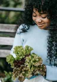 a young African American woman holding a bunch of lettuce in a community garden
