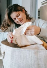 a woman with a phone at her ear holding a a laundry basket while laughing and holding a shirt