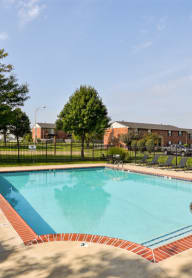 a swimming pool with a black fence behind it and a brick building in the background