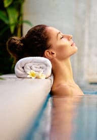 a woman in an infinity pool with her head in a bath tub with a towel