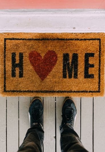 welcome mat with the word home and a heart. feet with sneakers next to the mat