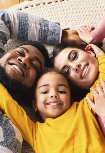 Mom, dad, and daughter laying down on the carpet and smiling