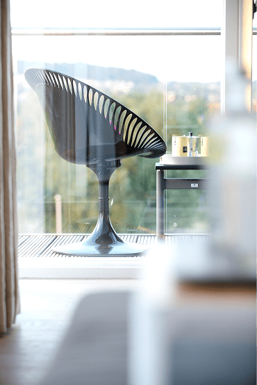 A black chair with a unique design sits in front of a window.