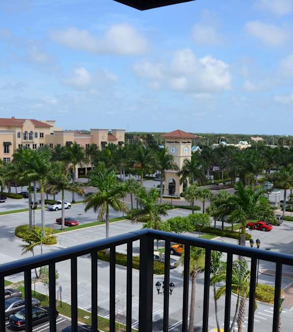 A view from a balcony overlooking a parking lot with palm trees.
