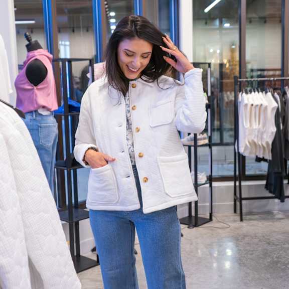 A woman in a white jacket and blue jeans is standing in a clothing store.