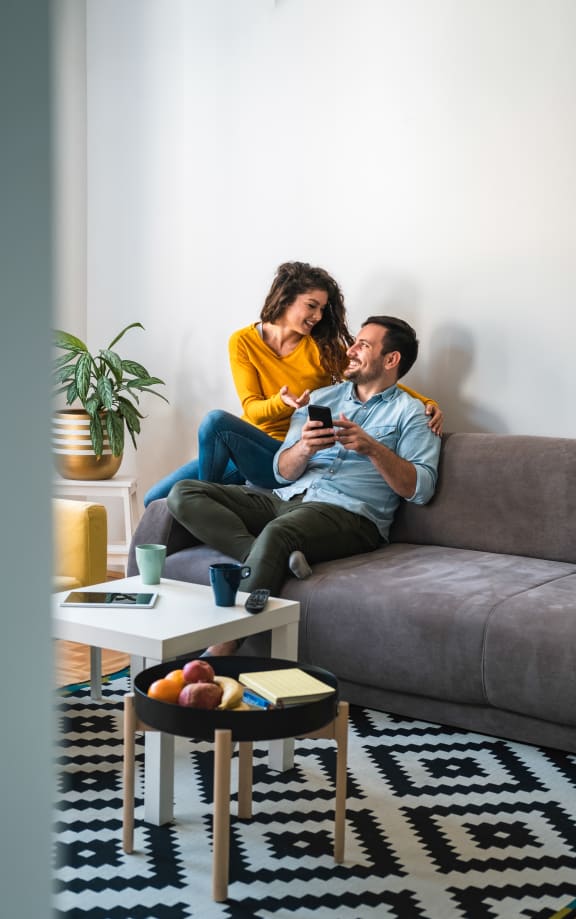 a couple sitting on a couch in a living room looking at a cell phone