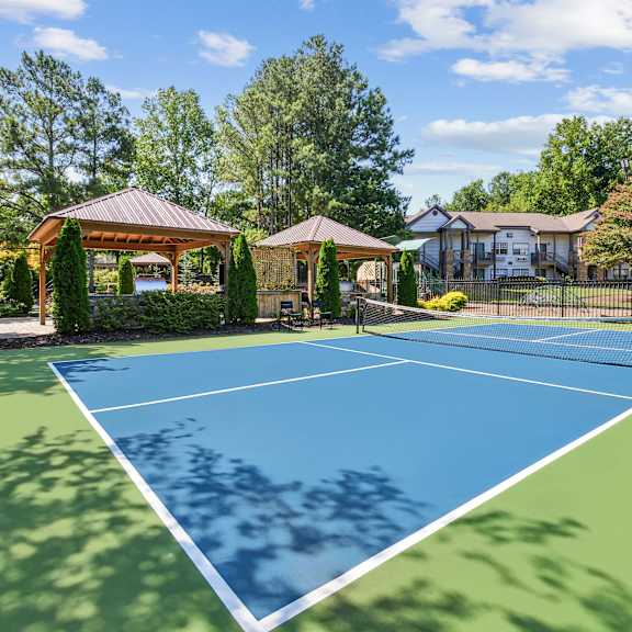 A tennis court is surrounded by trees and a gazebo.