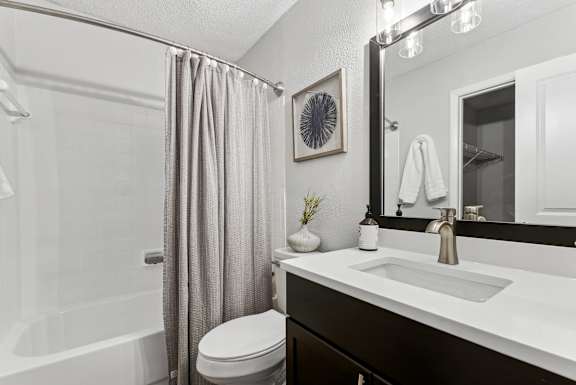 A bathroom with a white sink, toilet, and a shower with a grey curtain.