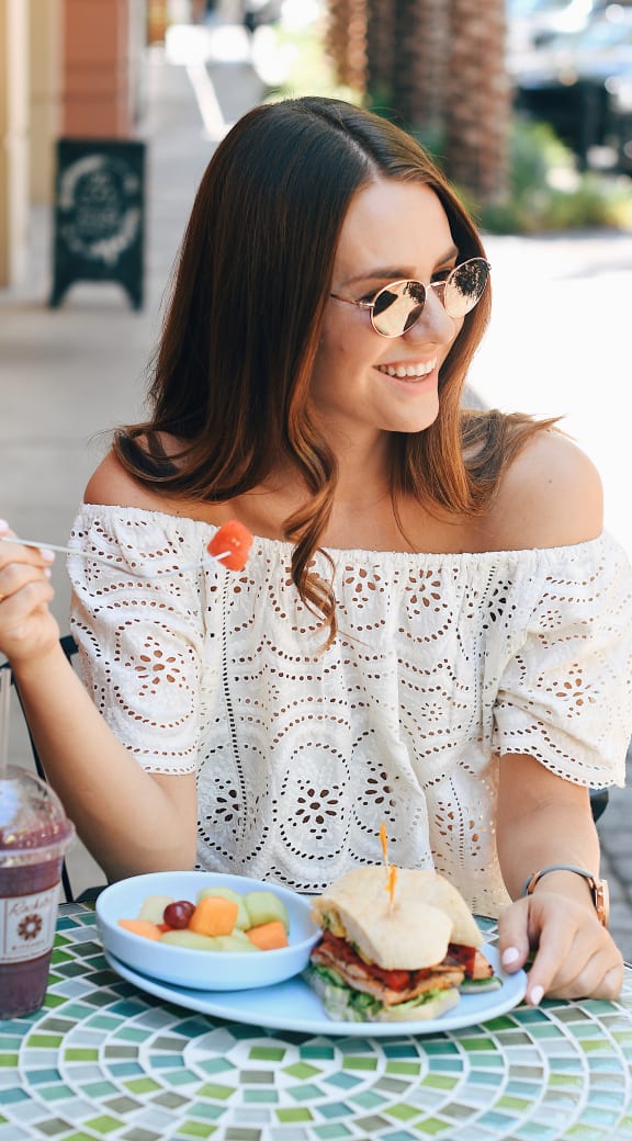 a woman sitting at a table with a sandwich and a smoothie