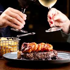 Two people toasting with wine glasses in front of a plate of food.