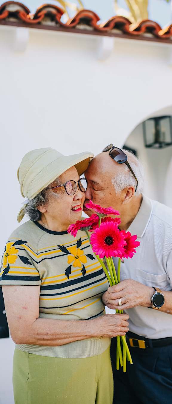 an older couple embraces while holding a bunch of flowers