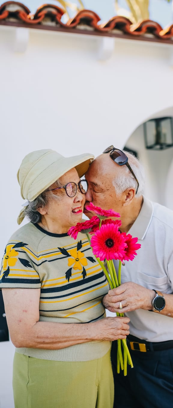 an older couple embraces while holding a bunch of flowers