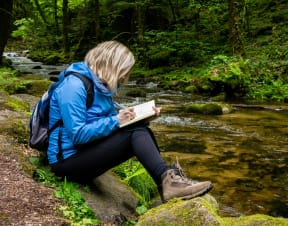 a woman sits on a rock next to a river and reads a book