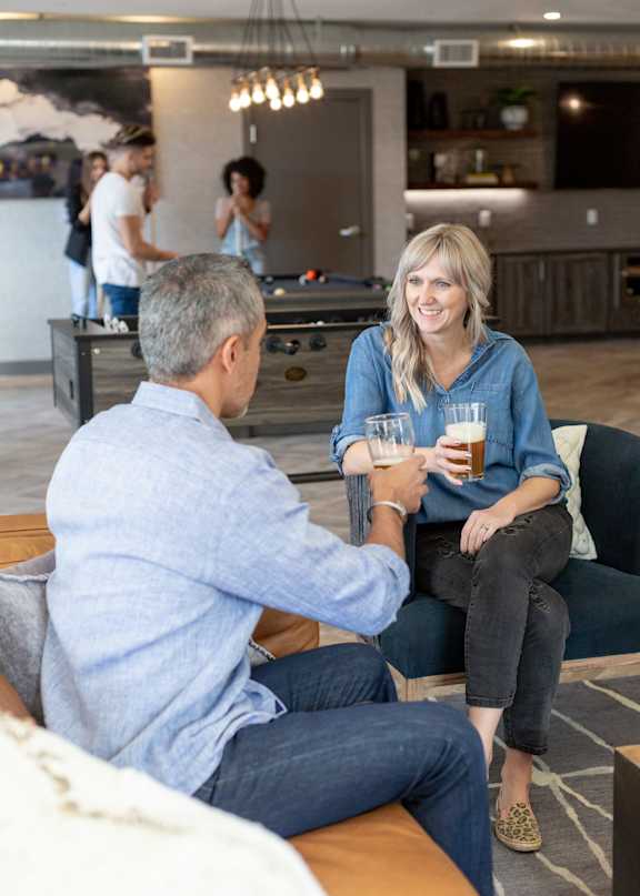 A man and a woman are sitting on a couch, having a conversation and enjoying drinks.