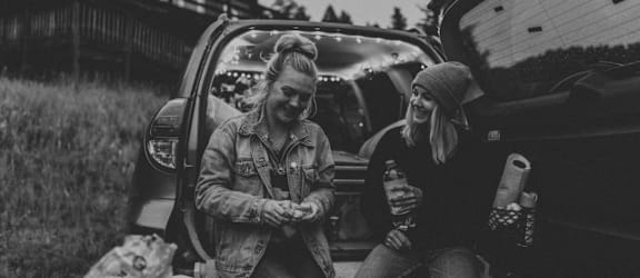 Two people sitting in the back of a car, one holding a drink and the other holding a bag.