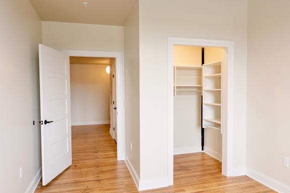 A white door is open to a hallway with a white wall and a white closet with shelves.