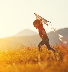 A child is running through a field with a kite.