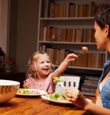 Little Girl Smiling while Eating Food with Her Mother