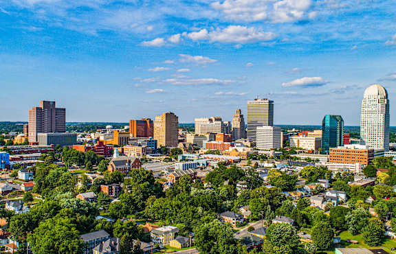 A cityscape with a mix of modern and older buildings, surrounded by greenery.
