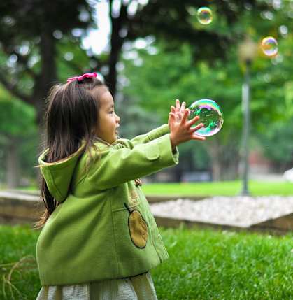 a young girl playing with soap bubbles in a park  at Pier Park Apartments, Oregon