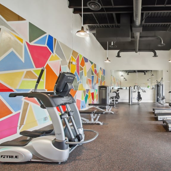 a gym with treadmills and weights and a colorful wall